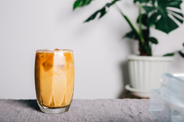 Iced coffee on a transparent glass plate on grey fabric on the\
table and monstera tree on pot houseplant decor at home summer\
drinkstudio photo