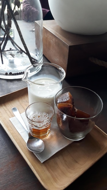 Iced coffee with fresh milk and liquid sugar served on wooden tray