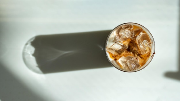 Iced coffee with ice cubes in glass on white background top view