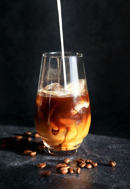 Iced coffee with ice cubes and pouring milk in a glass on a dark background