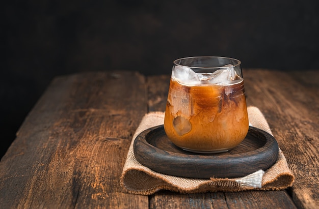 Iced coffee with milk on a brown wooden wall. Side view, copy space.