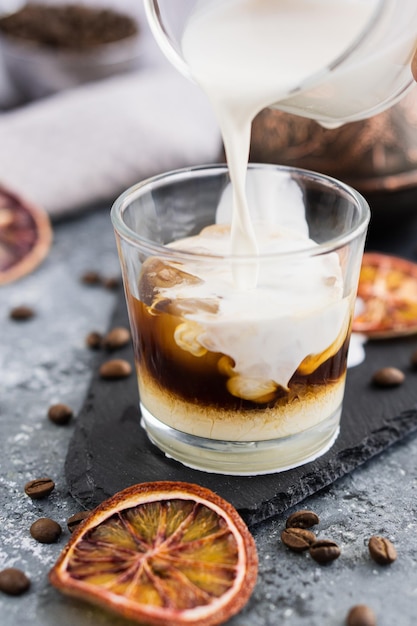 Iced coffee with milk Summer drink Pouring milk in coffee with ice cube on grey background