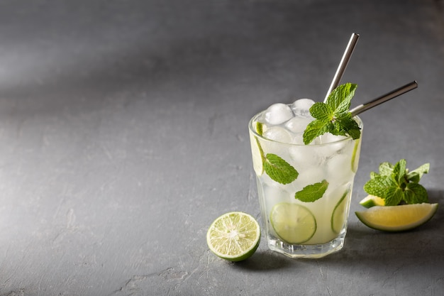 Iced cold summer homemade lemonade, infused water with lime and mint on grey background copyspace.