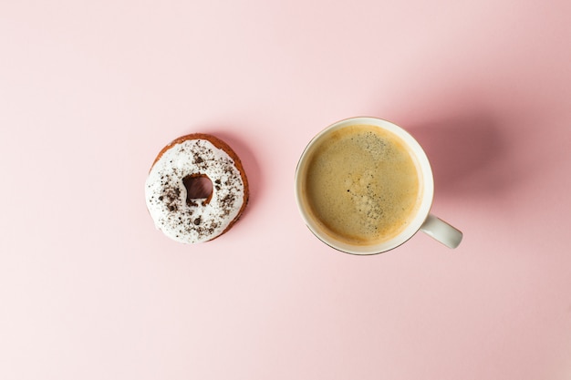 Iced donut with chocolate decor and cup of espresso on a pink pastel background