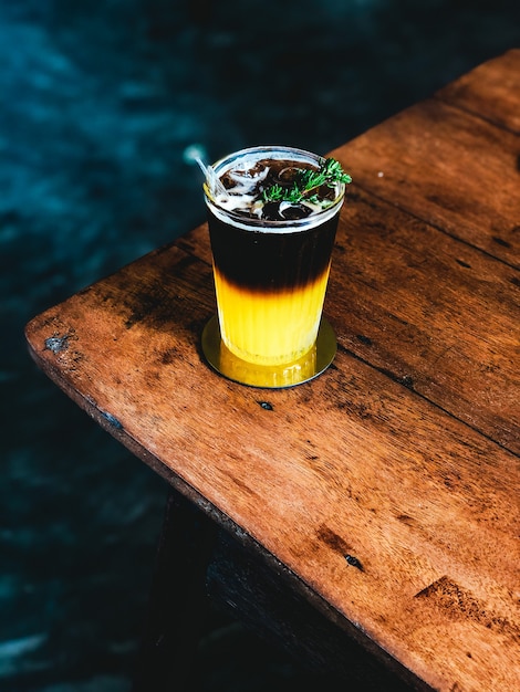 Iced fresh orange juice topped with espresso on wooden table in Modern cafe.