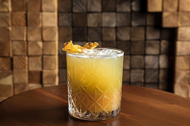 An iced fruity alcoholic cocktail in a lowball rocks glass garnished with dried pineapple on a wooden table and wooden background copy space