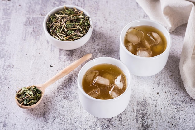 Iced green japanese hojicha tea in cups and leaves in a bowl on the table