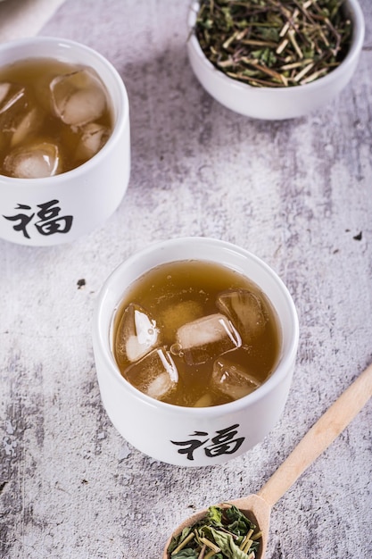 Iced green japanse hojicha thee in kopjes en bladeren in een kom op tafel verticaal zicht