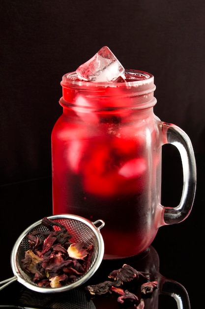 Iced hibiscus or karkade tea in the glass on the black  background.Close-up.