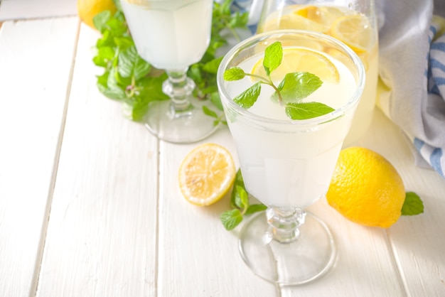 Iced homemade lemonade drink, limoncello liqueur cocktail decorated with mint and lemons on white wooden kitchen background