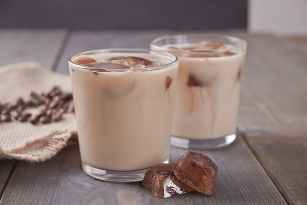 Iced latte coffee with ice cubes and coffee beans on a table.