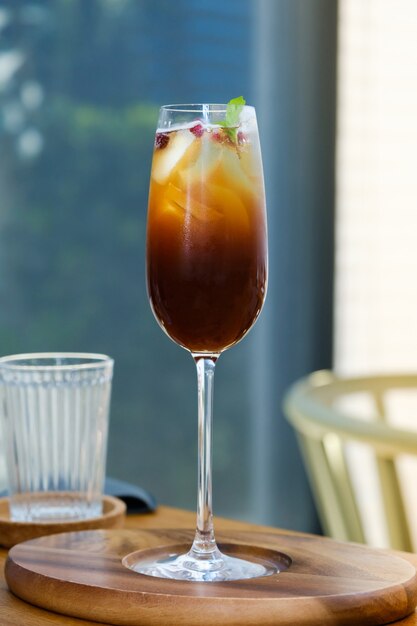 Iced mix fruit juice with black cold brew coffee in wine glass on wooden table at cafe.