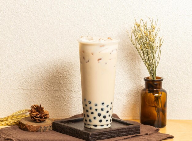 Photo iced pearl milk tea served in disposable glass isolated on wooden board side view of taiwanese ice drink