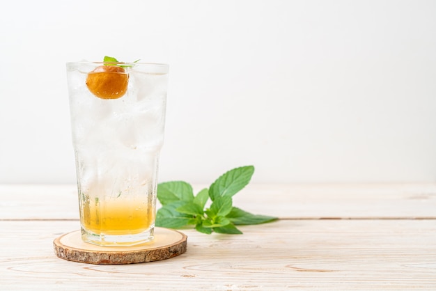 Iced plum juice with soda and peppermint on wood table