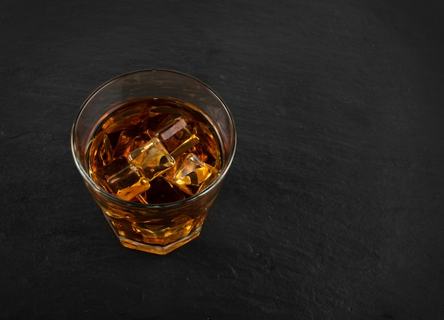 Фото Бокал для виски со льдом на натуральном черном каменном фоне