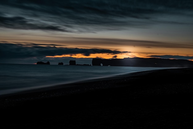 Фото Пейзаж исландии на закате на черном песчаном пляже с шелковой водой и горами с особыми формами на заднем плане