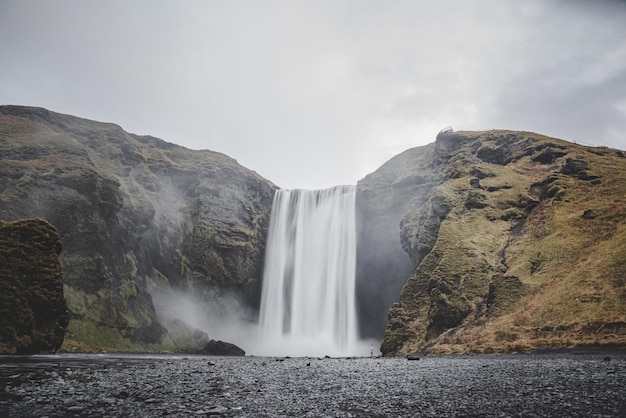 写真 背景に滝があるアイスランドの風景と灰色がかった空に黒い色の地球