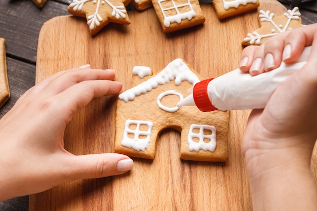 Foto glassa di pasticceria di natale. donna che decora i biscotti del pan di zenzero del miele sul bordo di legno, primo piano