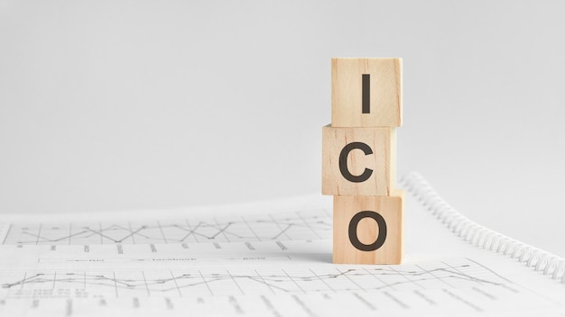 ICO - letters on wooden cubes. concept on cubes and diagrams on a green background. Business as usual concept image. space for text in left. front view. ICO - short for Initial coin offering