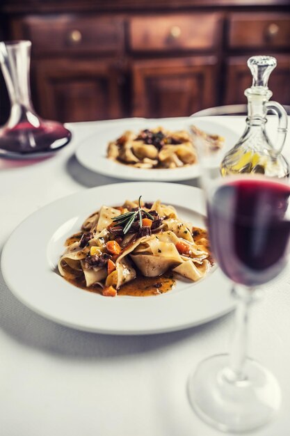 Photo idalian pasta pappardelle with beef ragout on white plate and red wine