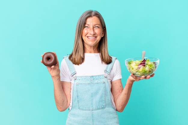 Donna graziosa di età inattiva con una ciambella e un concetto di dieta dell'insalata