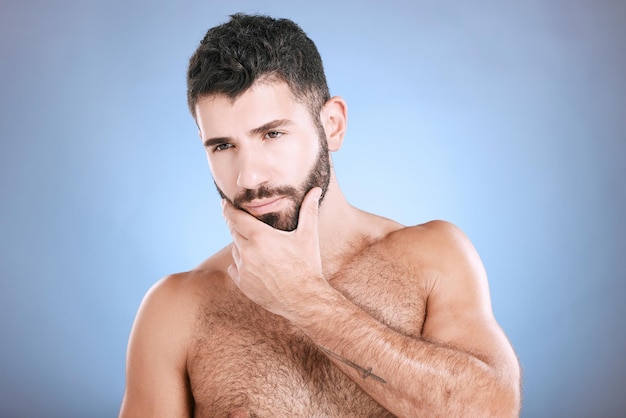 Foto idea bellezza e pelle con un modello uomo in studio su sfondo blu per il benessere naturale o la cura barba e cura della pelle del viso con un bel giovane maschio che pensa a cosmetici o trattamenti