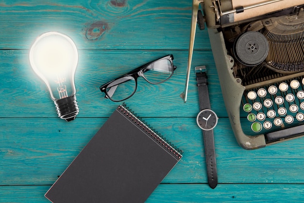 아이디어 개념 전구 빈티지 타자기 메모장 시계와 푸른 나무 책상에 안경