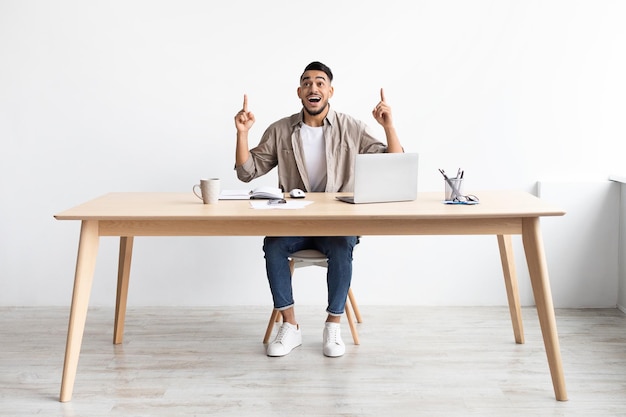 Idea concept excited bearded man pointing finger up at workplace