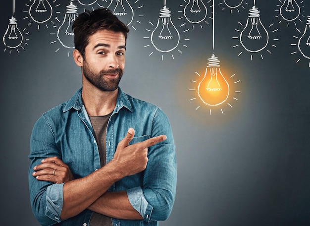 An idea is the seed of creation Studio portrait of a handsome young man pointing towards an illustration of a lit light bulb against a grey background