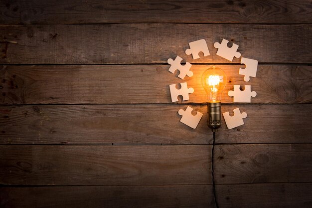 Idea and teamwork business concept vintage incandescent light bulb and jigsaw on the wooden background