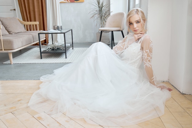 Ideal bride sitting on the floor, portrait of a girl in a long white dress.