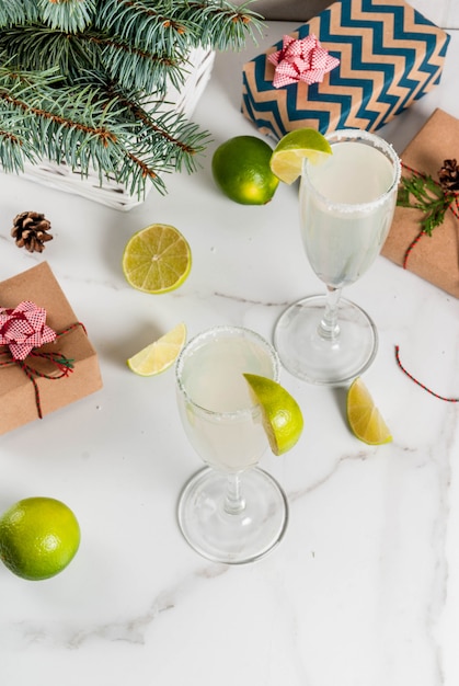 Ideas for Christmas and New Year drinks. Champagne Margarita cocktails, garnished with lime and salt. On white table with xmas decorations, copy space