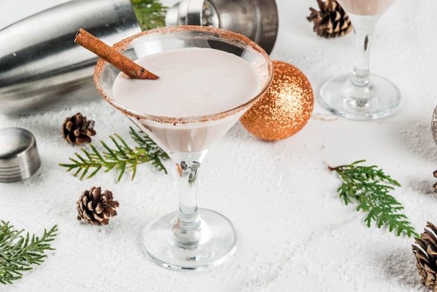 Ideas and recipes for Christmas drink. Eggnog martini, with cinnamon sticks, on white marble table with Christmas decoration, 