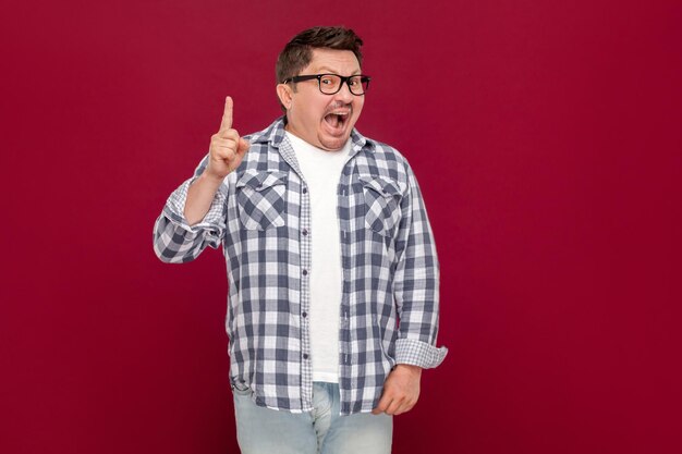 Idee. Portret van een geniale knappe zakenman van middelbare leeftijd in een casual geruit overhemd en een bril die staat te kijken en opgewonden is met zijn nieuwe idee. indoor studio opname, geïsoleerd op donker rode achtergrond.