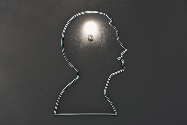 Ideeconcept met het profiel van de silhouetmens en gloeiende gloeilamp op donkergrijze muur