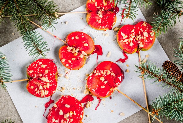 Ideeën voor de winter, kersttraktaties. snoepjes voor kinderen. chocolade appelplakken in rode karamel en noten. grijze stenen achtergrond, met kerstboom takken, bovenaanzicht