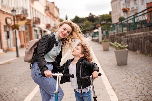 Identical mom and daughter with scooters in the city