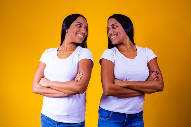 Identical twin sisters on yellow background with arms crossed