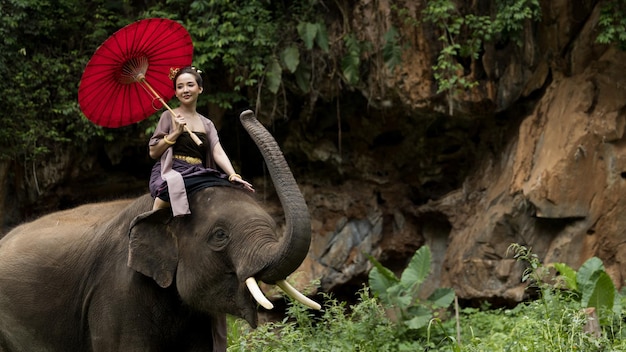 Identiteitscultuur van Thailand Thaise vrouw in traditionele Thaise cultuurkostuum Mooie aziatische vrouw draagt traditionele Thaise kleding met rode paraplu en berijdende olifant