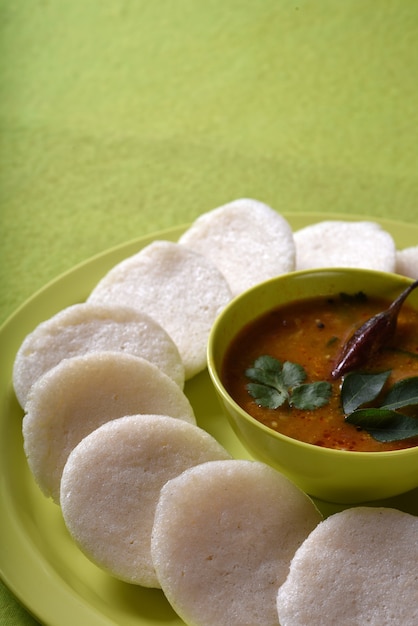 녹색 표면에 그릇에 Sambar를 넣은 Idli, Indian Dish : 인도 남부에서 가장 좋아하는 음식 rava idli 또는 세 몰리나 또는 멍청이, 삼바 및 녹색 코코넛 처트니와 함께 제공됩니다.