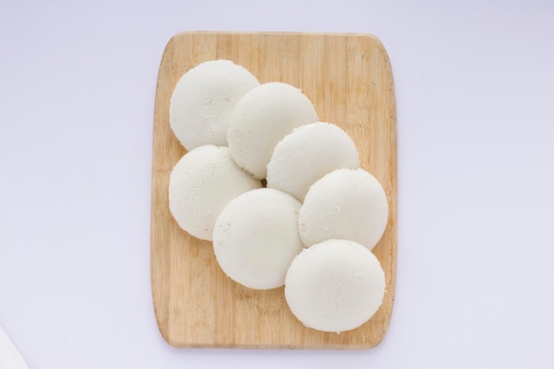 Idly 또는 Idli 남부 인도 메인 아침 식사 항목은 흰색 배경의 나무 바닥에 아름답게 배열되어 있습니다.