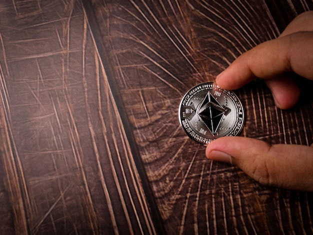 Iemand houdt met de ene hand zilveren ethereum digitale cryptomunt op houten tafel met kopieerruimte