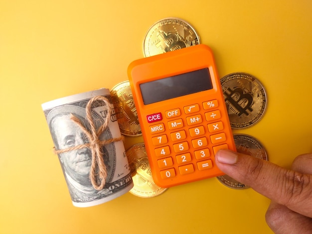 Iemand rekent met behulp van een rekenmachine met gouden bitcoin en bankbiljetten op een gele achtergrond