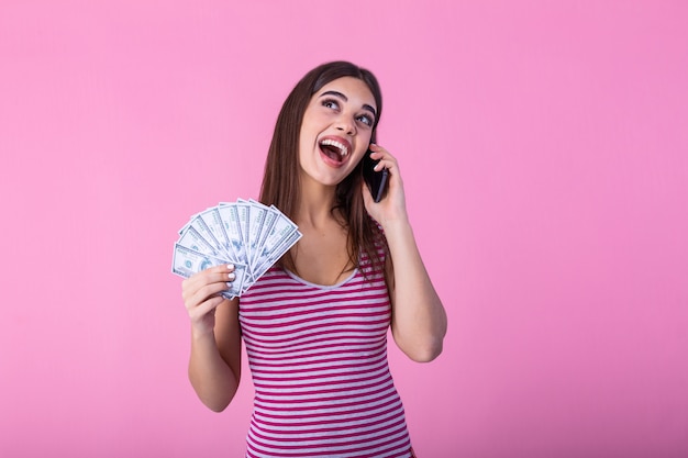 IExcited young woman holding money banknotes using mobile phone