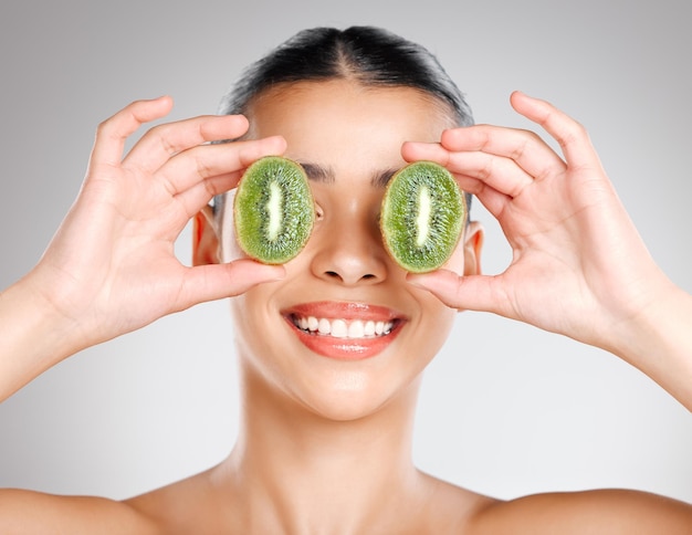 If its green its good for your skin Studio shot of an attractive young woman holding kiwi fruit to her face against a grey background