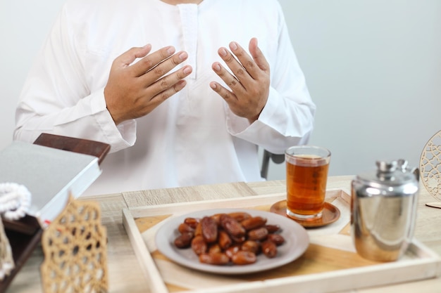 Iftar dish with muslim man hand praying to Allah Dates fruit with glass of hot tea on the table