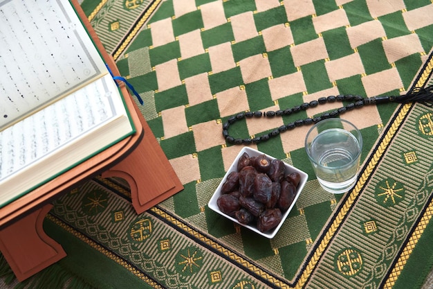 Iftar-tijd Gedroogde dadels, Heilige Koran glas water en tasbih op gebedskleed of sejadah. Artikelen die de vastenmaand vertegenwoordigen, Ramadan kareem-concept