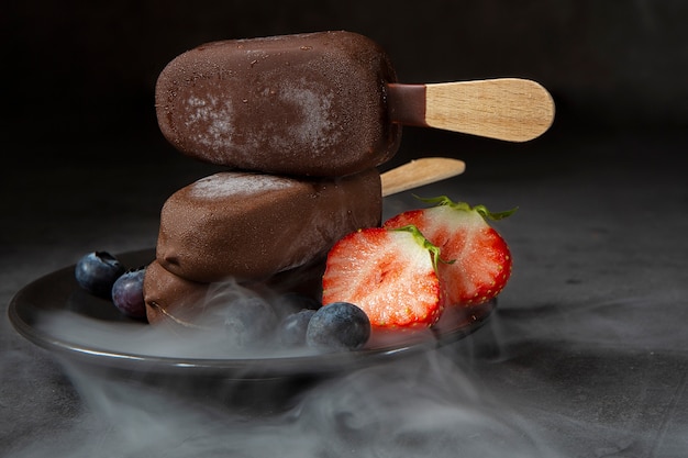 IJs op een chocoladestokje met aardbeien en bosbessen en met stoom. Zomerseizoen, hete zomer.