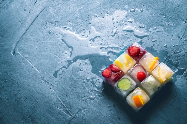 IJsblokjes met fruit op een steen blauwe ondergrond. De vorm van het vierkant. Munt, aardbei, kers, citroen, sinaasappel. plat lag, bovenaanzicht