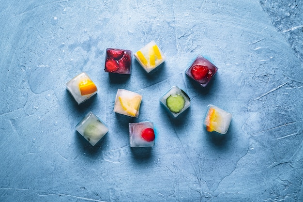 IJsblokjes met fruit op een steen blauwe ondergrond. Munt, aardbei, kers, citroen, sinaasappel. plat lag, bovenaanzicht